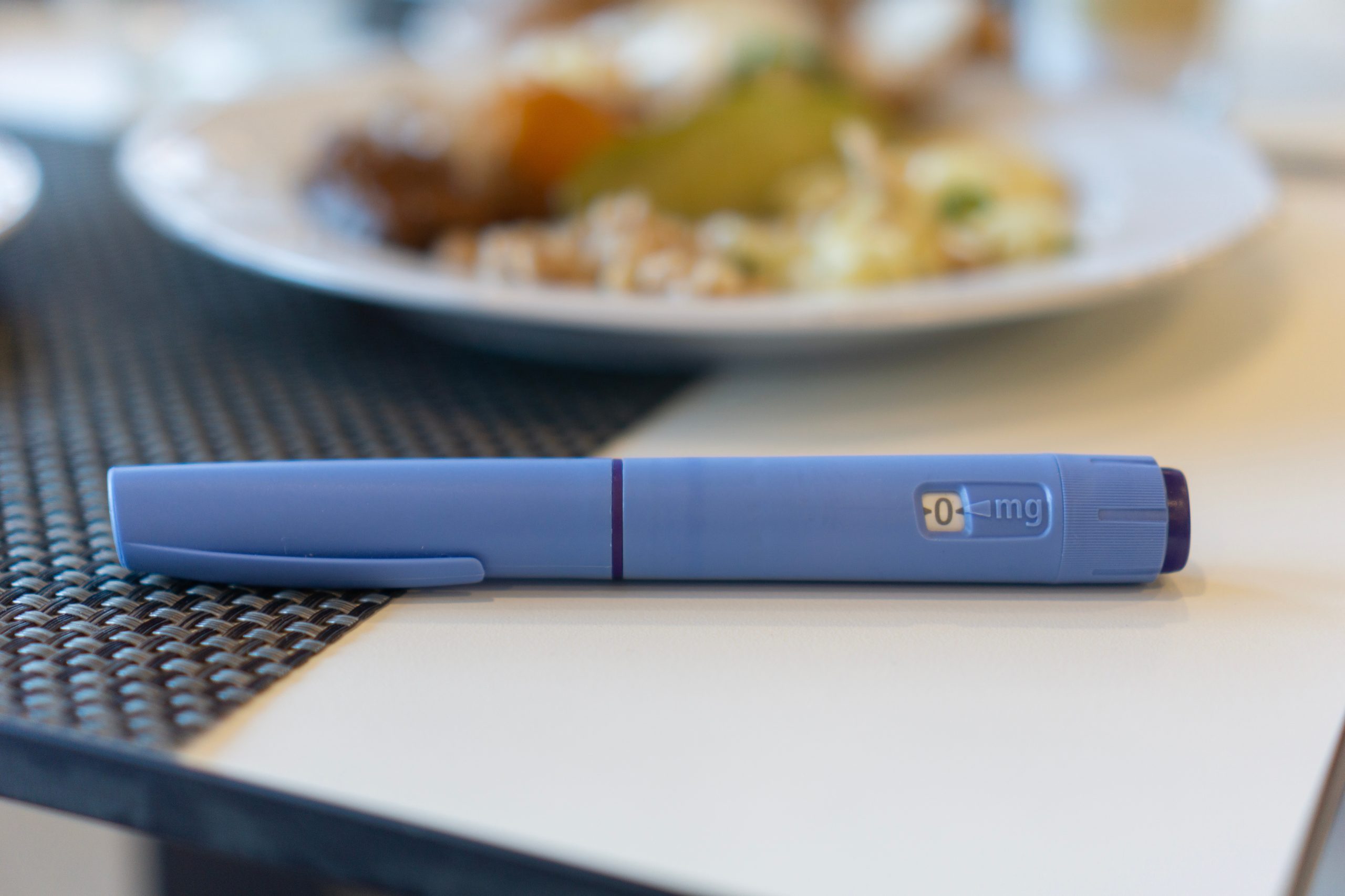 An Ozempic pen on a napkin next to a plate of unhealthy food, concept of medical treatment, diabetes management, and lifestyle choices